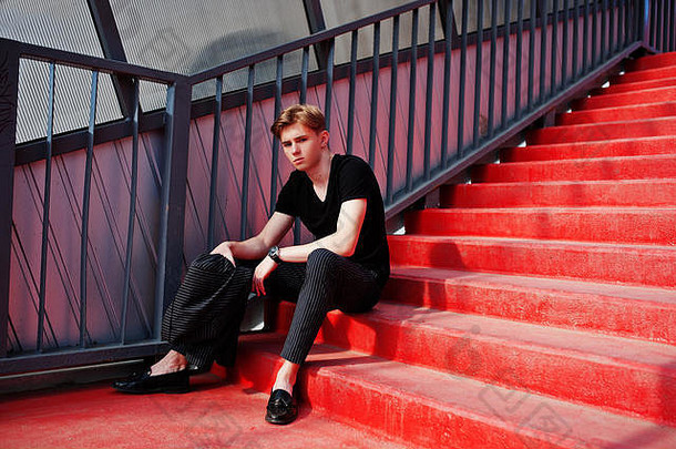 穿着黑色夹克的年轻时尚男子汉摆出街头户外的姿势。红楼梯上的惊人模特。