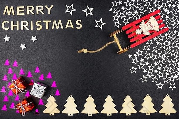 铭文“圣诞快乐”是由木制字母组成的，从上方平躺在黑色背景上。站在银色雪橇上的红色雪橇