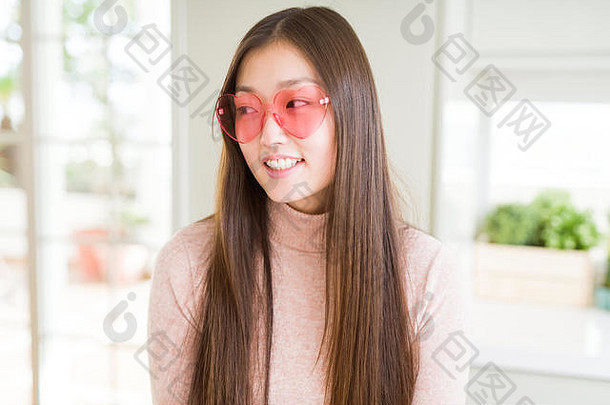 美丽的亚洲女人戴着粉色心形眼镜，微笑着看向一边，凝视着别处思考。