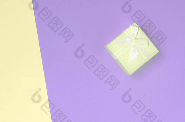 小黄色礼品盒位于时尚柔和的黄色和紫罗兰色纸的纹理背景上。