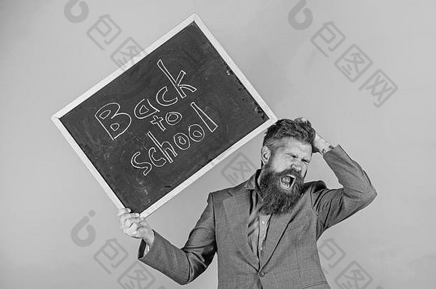 头发蓬乱的老师对开学感到紧张。留胡子的老师拿着写有铭文的黑板回到学校的绿色背景。继续工作。教授有压力的职业。
