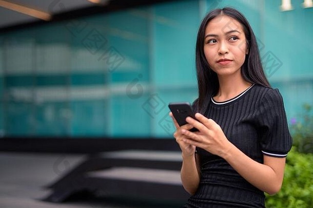 年轻的美丽的亚洲旅游女人思考电话购物中心在户外