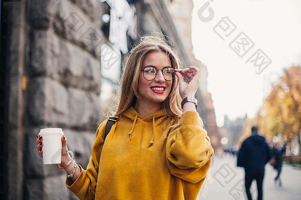 肖像：穿着鲜黄色运动衫的年轻时尚女生。一位年轻女子的特写肖像，她拿着一副眼镜，一边笑一边碰