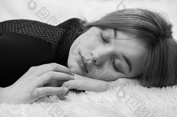 美丽悲伤的年轻女子睡在白色皮毛上，单色