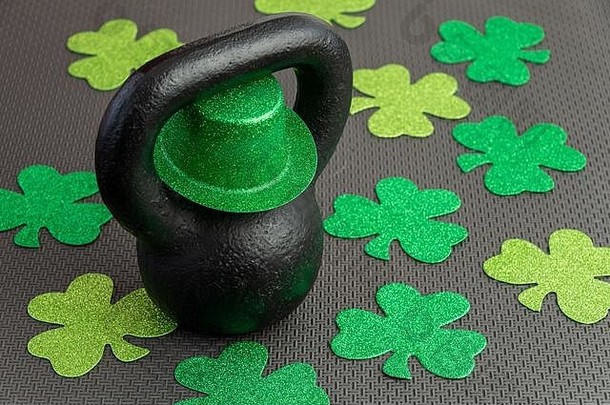 黑色的铁壶铃绿色小妖精他黑色的健身房地板上假期健身绿色三叶草