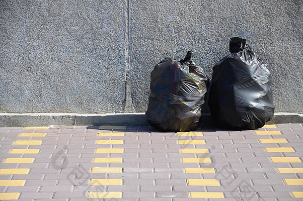 两个黑色垃圾袋放在城市水泥栅栏铺着瓷砖的街道地板上。污染垃圾