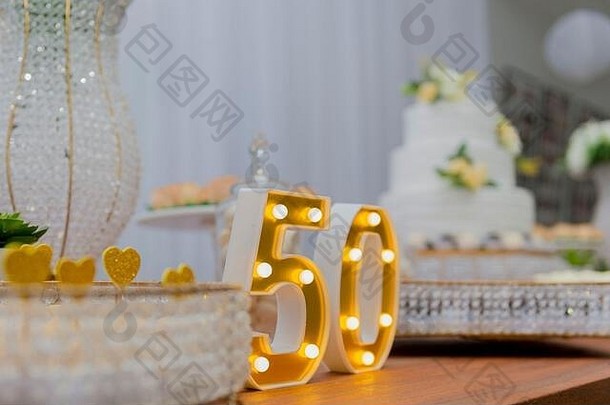 一个为50周年而装饰的漂亮蛋糕。餐桌生日派对，双层白色蛋糕装饰着黄玫瑰和绿叶麸皮