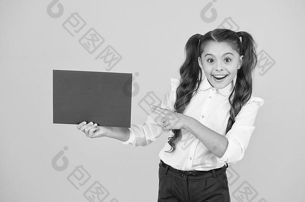 展示你的产品。快乐的小女孩用手指着黄色背景上的空红纸做产品广告。返校产品。引起对产品或事件的注意，复制空间。