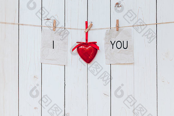 红心和旧纸，上面写着“我爱你”，挂在晾衣绳上，背景是白色的木头。