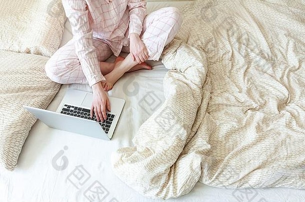 移动办公室在家里。穿着睡衣的年轻女子坐在家里的床上用笔记本电脑工作。生活方式女孩在室内学习。自由职业者商业隔离概念