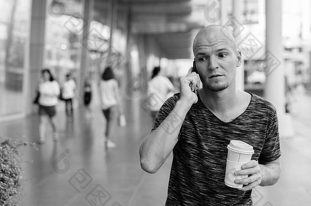 年轻的英俊的秃男人。持有咖啡会说话的电话购物中心