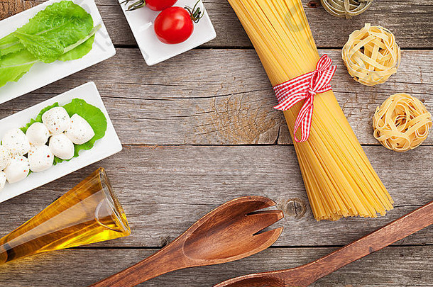 木桌背景上的西红柿、马苏里拉、意大利面和绿色沙拉叶