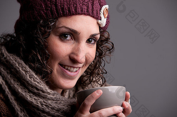 面带微笑的女人，满满一大杯热饮，穿着温暖的衣服，比如帽子和围巾