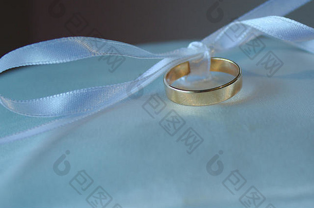 一条绑在蝴蝶结上的白丝带把结婚戒指放在枕头上。
