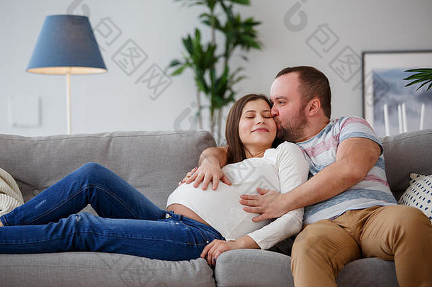 在灰色沙发上拥抱孕妇和男子的照片