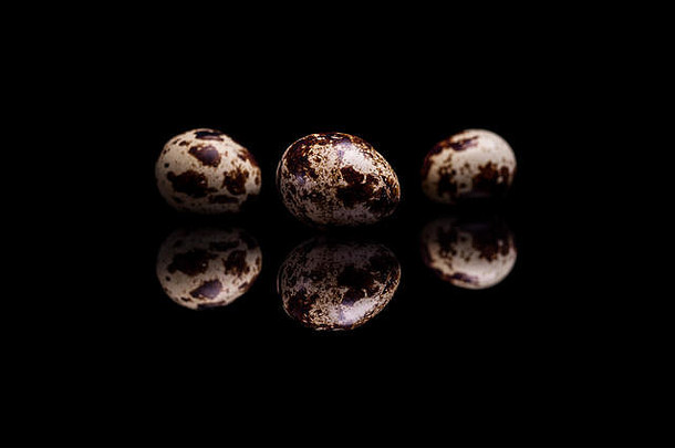 在黑色反光背景上分离出三个鹌鹑蛋