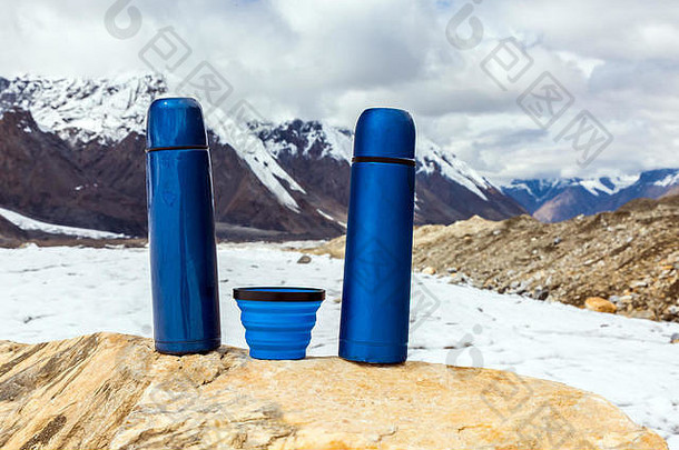 两个蓝色旅行热水瓶和石头上的杯子