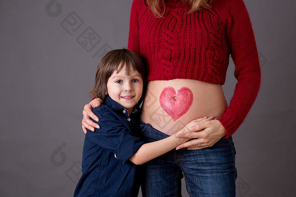 美丽的学龄前儿童，拥抱着怀孕的妈妈，快乐地期待着成为大哥哥。红心画在母亲的肚子上，孩子亲吻她的小b
