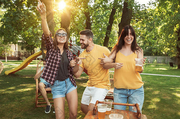 一群快乐的朋友在阳光明媚的日子里举行啤酒和烧烤派对。一起在户外的林间空地或后院休息。欢庆、放松、欢笑。夏季生活方式，友谊理念。