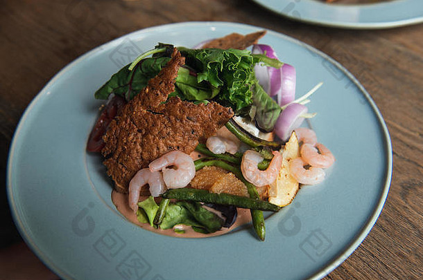 美味的沙拉配虾、生菜、梭子鱼、洋葱和芦笋。木制桌子上的绿松石板。