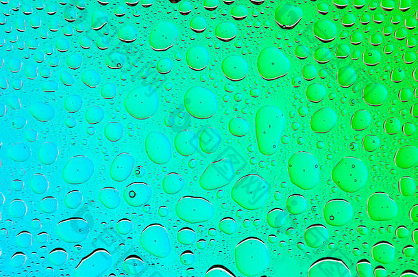 绿色和蓝色渐变背景上的水滴特写，覆盖着水滴凝结。