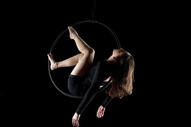 优雅的空中舞者一名女子，她用一个孤立在黑色地板上的铁环表演