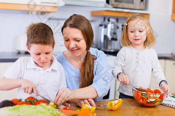 年轻的母亲和她的两个孩子在做蔬菜沙拉