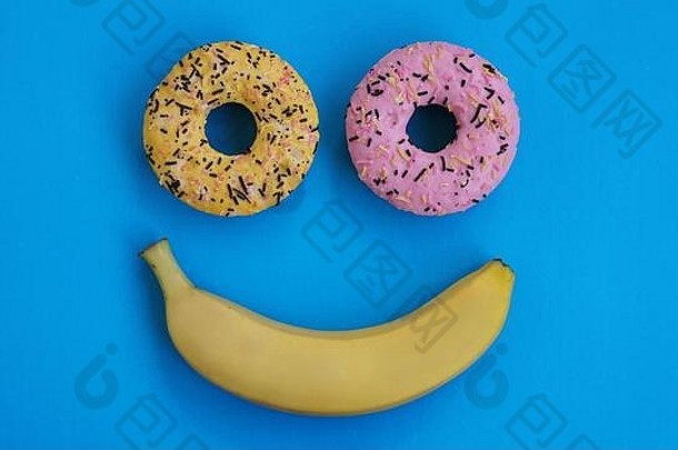 甜甜圈香蕉谎言蓝色的表面形成抽象表情符号微笑前点