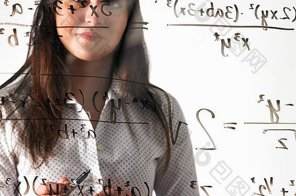 一个年轻的女人看着一个数学方程式，这个方程式用黑色记号笔写在透明的透明墙上