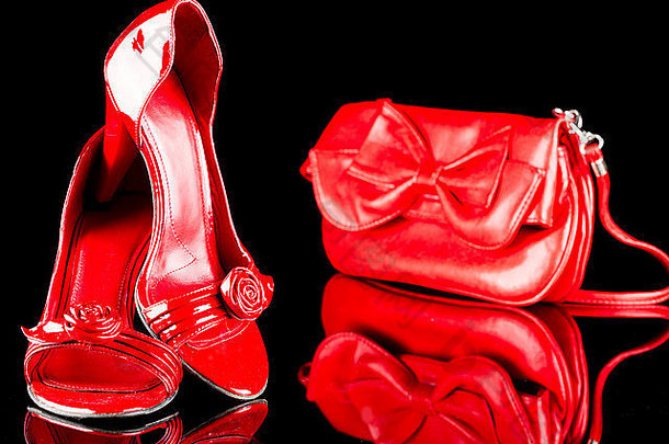 奢华的红色高跟女鞋和黑色背景的包。反射