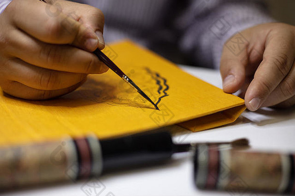 活页夹在他的工作室里，在一本精装书的黄色封面上用手画一幅书法图案，在他的手上画一个特写