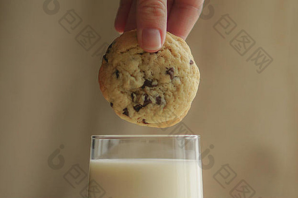 一个女孩手里拿着一块饼干，放在装满牛奶的杯子上面
