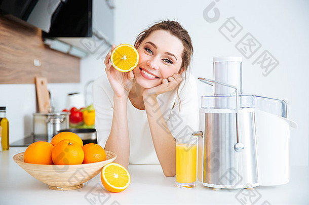 开朗漂亮的年轻女子坐在厨房里拿着一半的橘子
