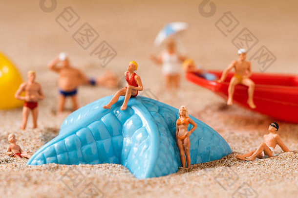 在海滩的沙滩上，一些穿着泳衣的人们在一只蓝色塑料海星和一把红色玩具铲旁放松