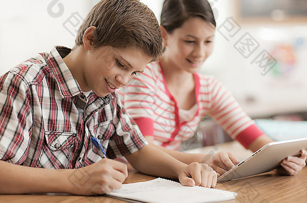 两个孩子，一个男孩和一个女孩坐在教室里，共享一个数字平板电脑。