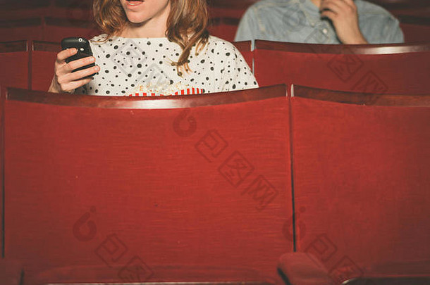 一名年轻女子在剧院里用手机，一名男子坐在她身后
