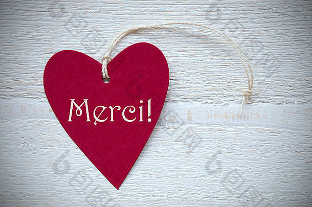 一个红色心形标签或标签，白色木质背景上有白色丝带，法文文字Merci表示“快乐，谢谢”，复古Ret
