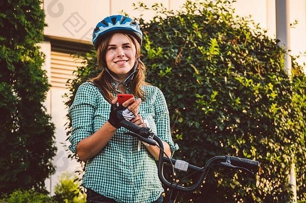 一个拿着手机的快乐女孩的肖像。快乐微笑的学生在户外智能手机上使用自行车共享应用程序。都市生活时尚时髦