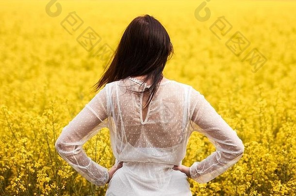 女人白色衣服站回来黄色的油菜籽场春天概念