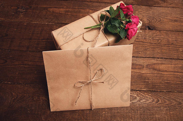 用<strong>牛皮纸包装</strong>的礼物，信封附近顶部有玫瑰花