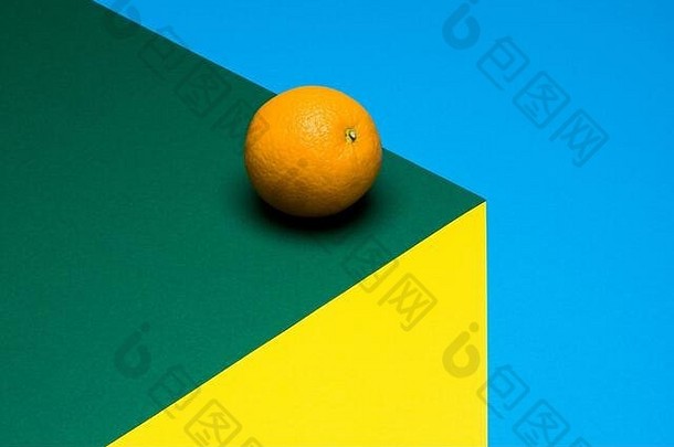 多色背景上的橙色果实，彩色纸上的半个橙色。空间。