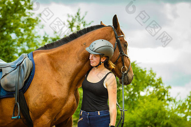 爱护动物，爱和友谊的理念。在阳光明媚的日子里，戴着头盔的骑师少女抚摸并拥抱着棕色的马