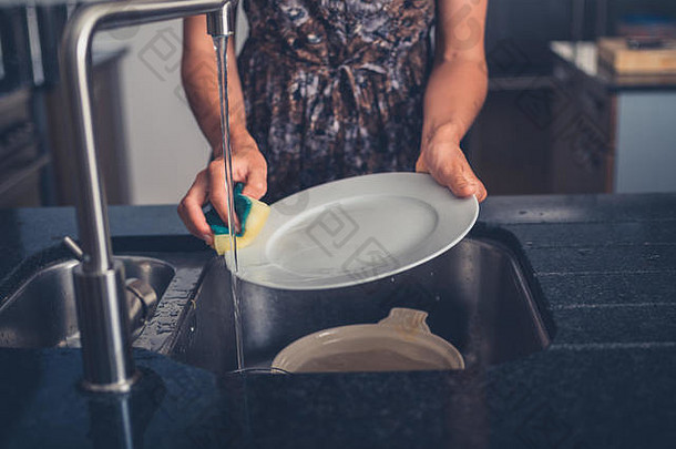 一位年轻女子正在她的现代化厨房的水槽旁洗碗