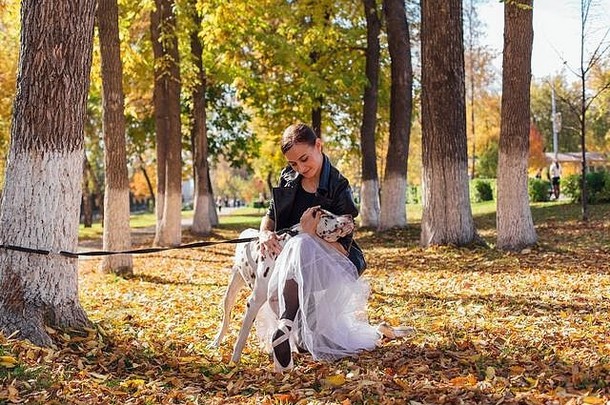 芭蕾舞女演员和达尔马提亚狗在公园里。穿着白色芭蕾舞裙、黑色皮夹克和尖头鞋的女芭蕾舞演员在秋季公园拥抱
