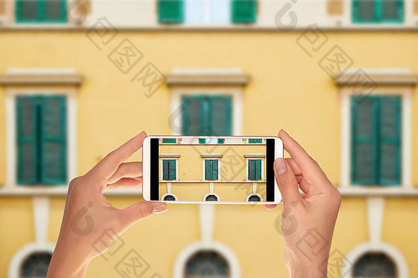 一名游客正在用手机拍摄意大利罗马一座建筑正面窗户上的图案