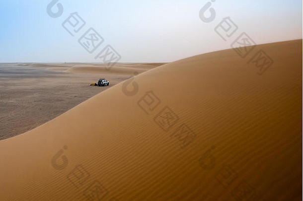 清晨，在苏丹撒哈拉沙漠的一个大沙丘上，有一种沙漠的气氛，背景是帐篷和吉普车