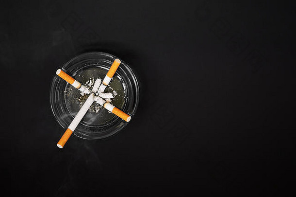 烟灰缸中的香烟十字架，深色背景。世界无烟日概念。吸烟致死。拷贝空间