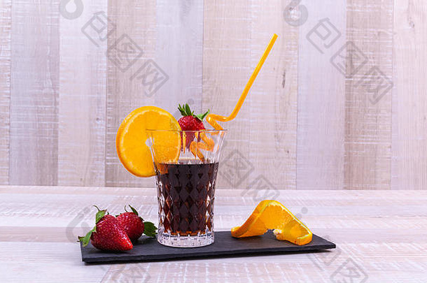 <strong>可乐倒</strong>进玻璃杯，饮料和水果在一块黑色的石板上，背景为浅色木质