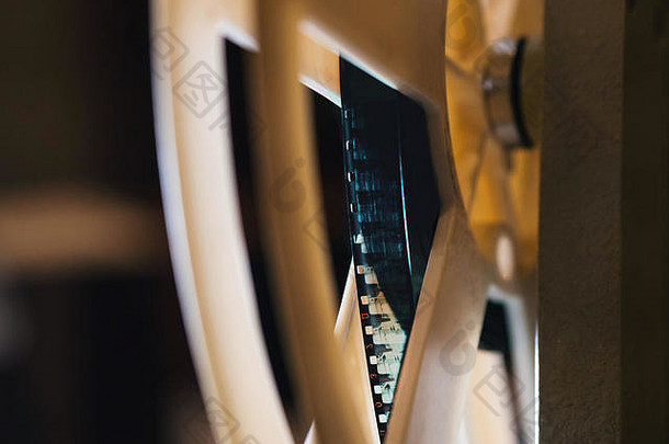 一台老式的超8mm老式电影放映机的正视图，在一个黑暗的房间里投射出一束光，旁边是一堆散开的电影卷盘。