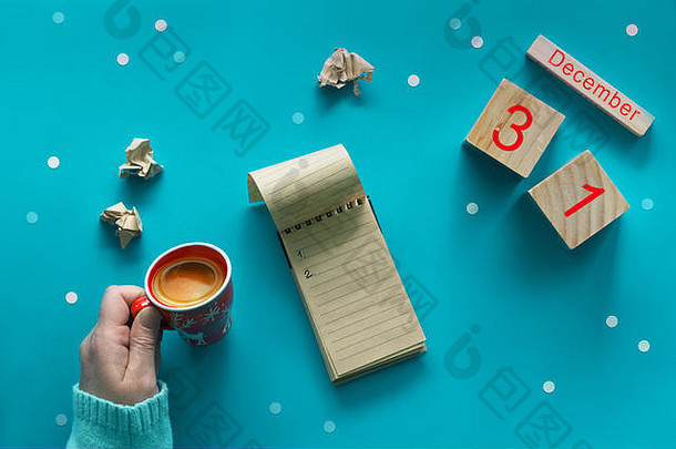 在蓝色粉彩桌面上，用钢笔、手工纸笔记本、木制<strong>日历</strong>和咖啡制作圣诞活动清单。平铺样式，蓝色纸背景，带